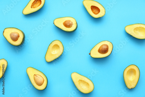 Halves of fresh avocados on color background