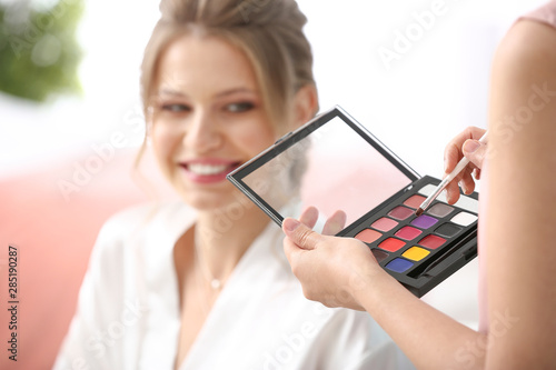 Professional makeup artist working with young bride at home, closeup