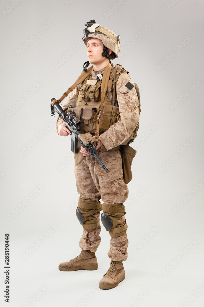 Soldier in US marines uniform with rifle on light grey background, studio shot Soldier in US marines uniform with rifle on light grey background, studio shot