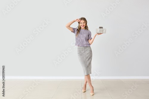 Beautiful young woman with gift box against light wall