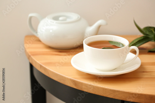 Cup of hot beverage and teapot on table