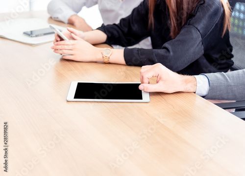 Closed up hands of business people with tablet pc with blank screen while sitting at the wooden table work in meeting room.Communicates brainstorming using a tablet computer technology concept.