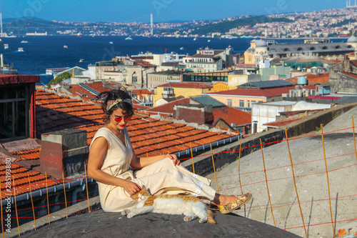 Woman touching yellow cat at the roof with bosphorus background in Istanbul