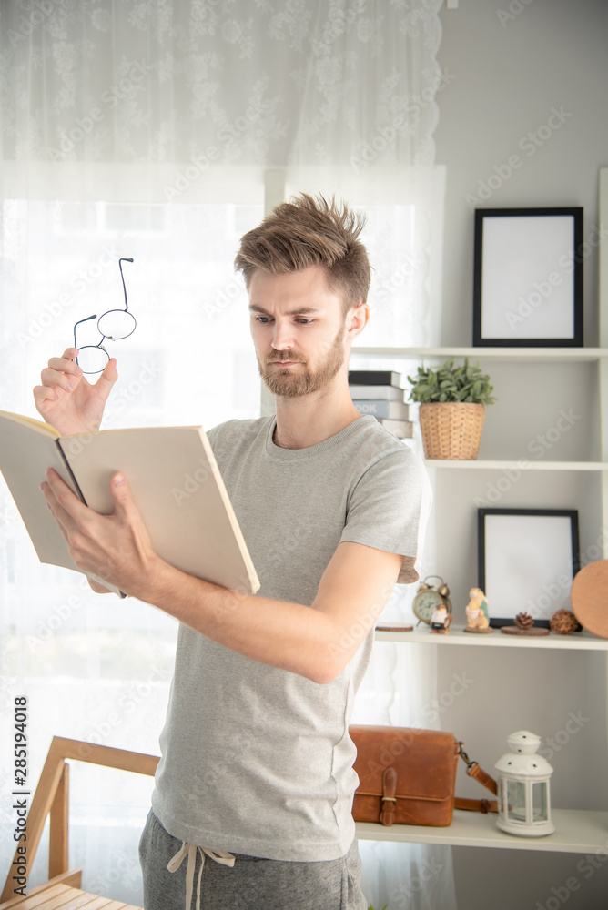 Handsome young caucasian Man reading a book in his living room ,feeling serious and surprised Handsome young caucasian Man reading a book in his living room ,feeling serious and surprised