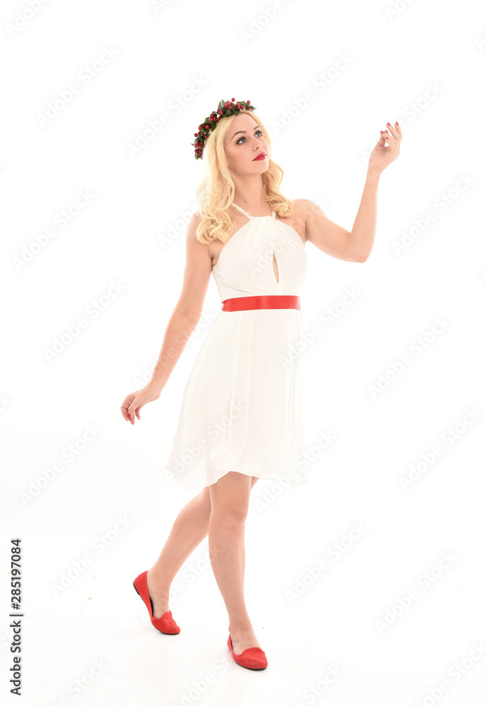 full length portrait of blonde girl wearing a white dress and flower crown.  Standing pose, isolated against a  white studio background.