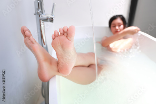 sexy and naked asian woman, long hair taking shower in white bathtub, focus on her feet