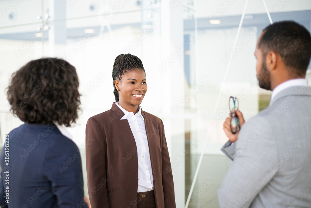 Multiethnic group of partners meeting in office hallway. Young black business woman standing with smiling and talking to colleagues. Corporate meeting concept Multiethnic group of partners meeting in office hallway. Young black business woman standing with smiling and talking to colleagues. Corporate meeting concept
