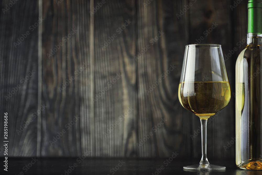 Transparent bottle of white dry wine on the table. White wine glass on a wooden background. Transparent bottle of white dry wine on the table. White wine glass on a wooden background.