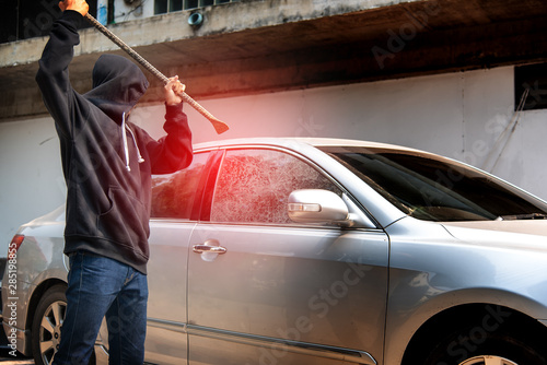 Car thief stealing to break glass into a car .Masked hide face man ,robber dressed in black holding crowbar into car damage glass window of car. © kittipong