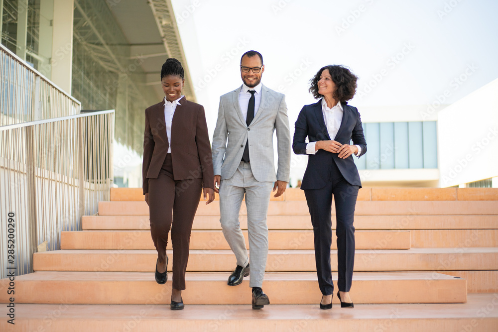 Happy businesspeople walking near office building. Team of business man and women going down stairs, talking, laughing. Teamwork concept Happy businesspeople walking near office building. Team of business man and women going down stairs, talking, laughing. Teamwork concept