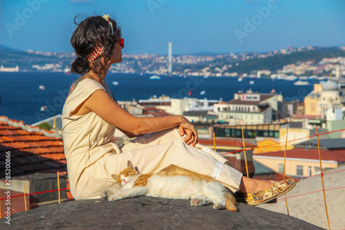 Woman touching yellow cat at the roof with bosphorus background in Istanbul