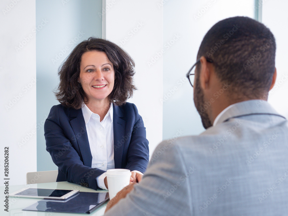 Obraz premium Smiling female job candidate talking to employer during interview. Business man and woman sitting at meeting table and talking. Career concept