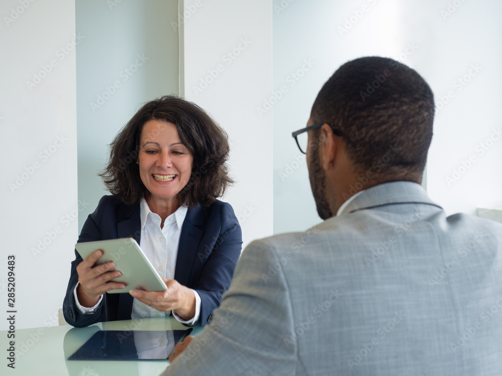 Business professionals meeting in conference room and discussing project. Business woman sitting against male colleague, using tablet and smiling. Wireless technology concept Business professionals meeting in conference room and discussing project. Business woman sitting against male colleague, using tablet and smiling. Wireless technology concept