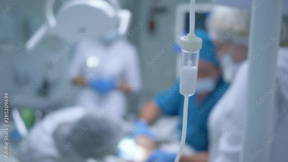 medical intravenous dropper, during operation a group of doctors treat patient with general anesthesia in a modern stamotological clinic out of focus medical intravenous dropper, during operation a group of doctors treat patient with general anesthesia in a modern stamotological clinic out of focus