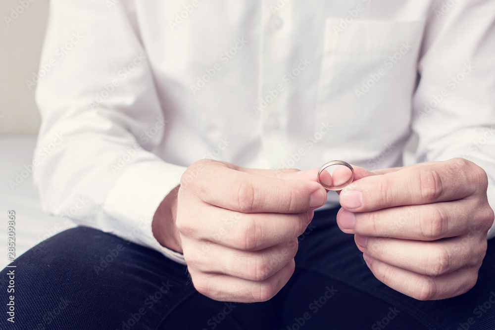 Husband holding wedding ring, man sits in the marital bedroom, closeup, cropped image, toned. The concept of divorce and family disintegration Husband holding wedding ring, man sits in the marital bedroom, closeup, cropped image, toned. The concept of divorce and family disintegration