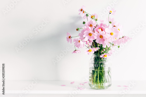 Canvas Fresh summer bouquet of pink cosmos flowers in glass vase on white wood shelf on white wall background