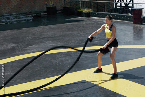 Sport woman doing battle ropes exercise workout at gym