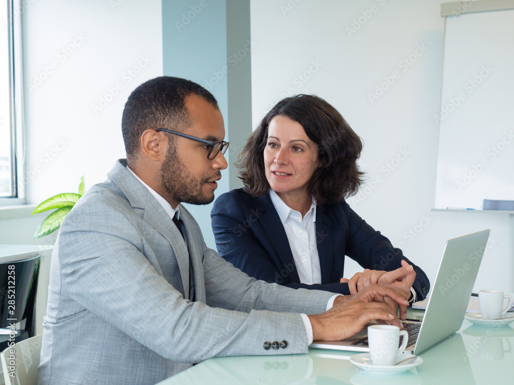 Senior employee teaching newcomer. Business man and woman using laptop together and talking in boardroom. Working on project concept Senior employee teaching newcomer. Business man and woman using laptop together and talking in boardroom. Working on project concept