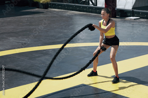 Sport woman doing battle ropes exercise workout at gym