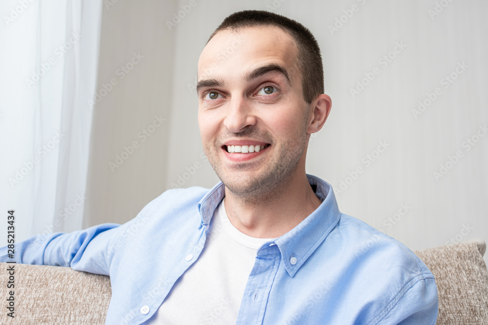 Young attractive man sitting at home, guy smiles. Portrait, toned Young attractive man sitting at home, guy smiles. Portrait, toned