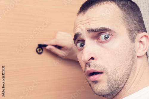 Scared man at the front door, peephole of front door, portrait, closeup, toned