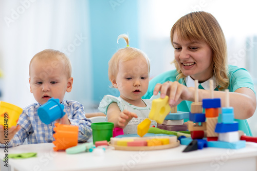 Nursery teacher looking after children in daycare. Little kids toddlers play together with developmental toys. Babies with caregiver in creche