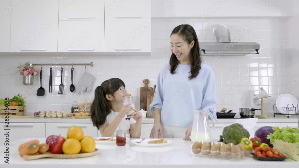 Happy Asian family Mother and Little girl are eating breakfast in the kitchen at home. Bread with jam and drinking milk. Healthy food concept Happy Asian family Mother and Little girl are eating breakfast in the kitchen at home. Bread with jam and drinking milk. Healthy food concept
