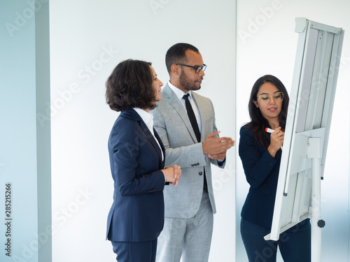 Young female professional presenting report to colleagues. Business woman drawing on board, her two coworkers looking at drawing. Demonstration concept