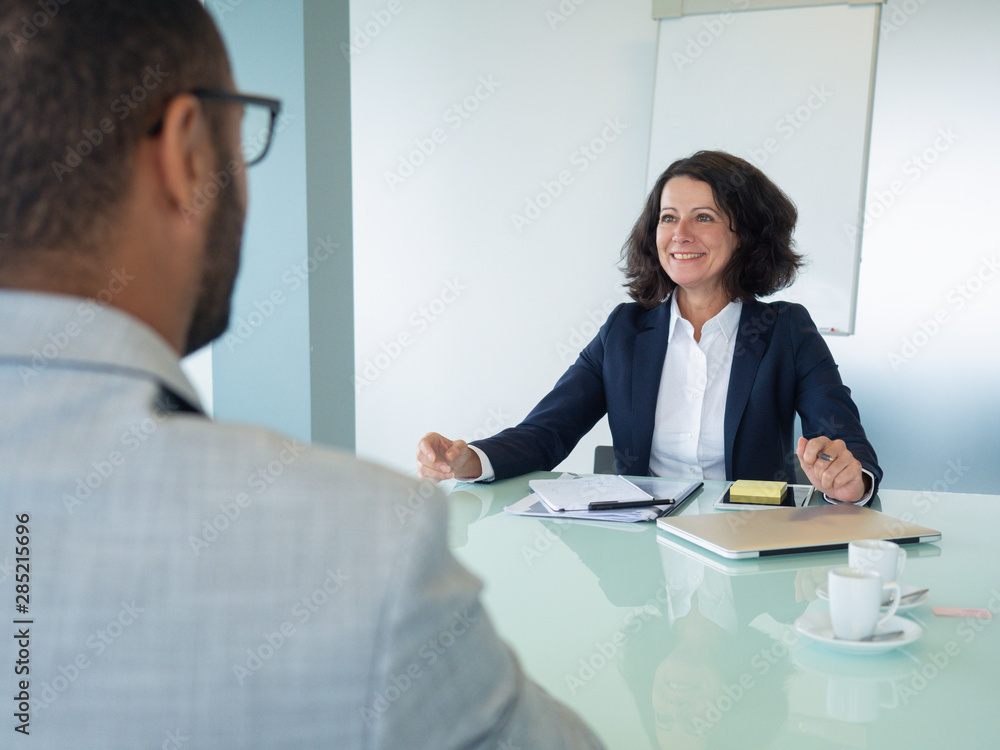 Happy corporate trainer telling newcomer about work at company. Business man and woman sitting at meeting table opposite of each other. Intern training concept Happy corporate trainer telling newcomer about work at company. Business man and woman sitting at meeting table opposite of each other. Intern training concept
