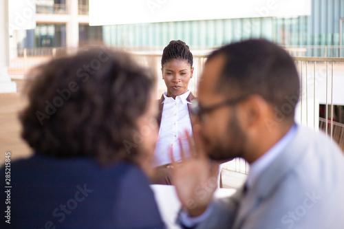 Male and female employees whispering gossips about African American colleague. She staring at them with angry. Gossips concept photo