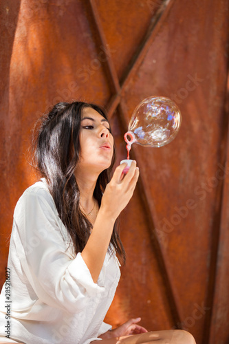 Beautiful young woman with white blouse blowing soap bubble..
