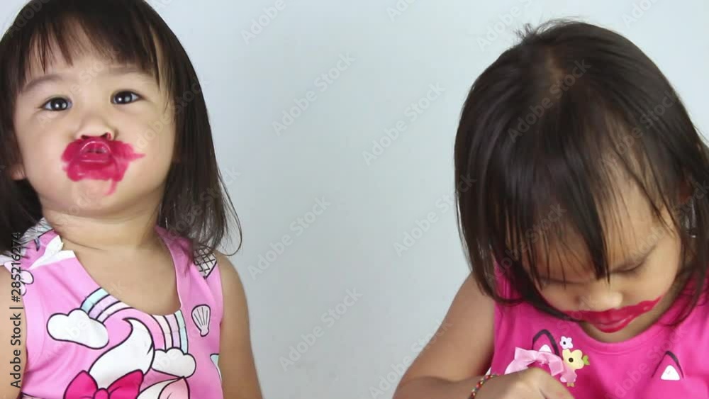 Happy Asian child girl with her sister apply red lipstick on lips and make kiss to camera.