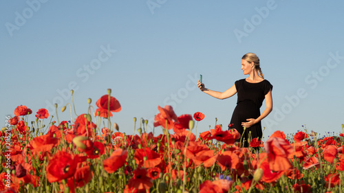 Junge Frau fotografiert sich mit Ihrem Smartphone im Mohnfeld