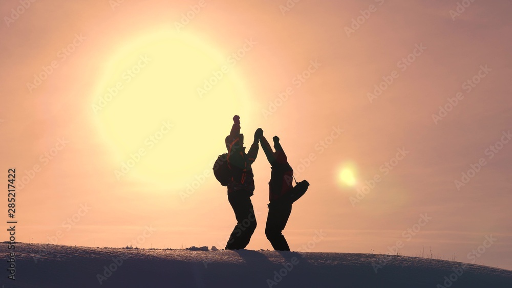 Tourists come to top of snowy hill and rejoice at victory against backdrop of yellow sunset. travelers met on top of success. teamwork and victory. ecological tourism