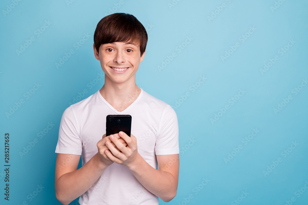 Photo of tight smiling boy taking smartphone with his own hands for first time while isolated with blue background Photo of tight smiling boy taking smartphone with his own hands for first time while isolated with blue background