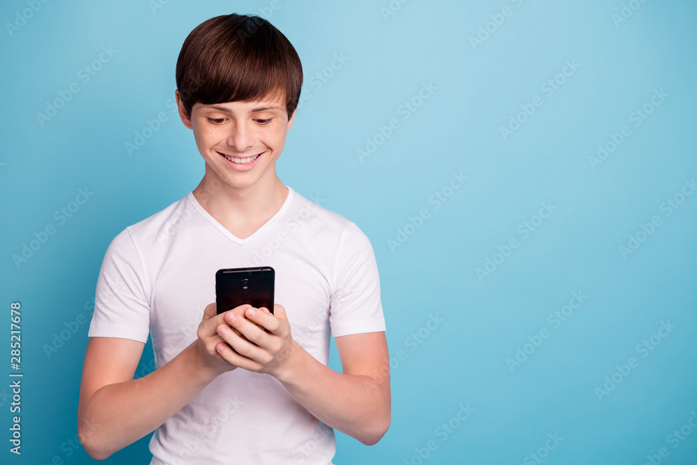 Photo of smiling rejoicing boy having received message from his classmate girl he has liked since they went to kindergarten while isolated with blue background Photo of smiling rejoicing boy having received message from his classmate girl he has liked since they went to kindergarten while isolated with blue background