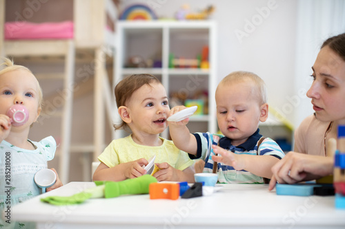 Adorable kids toddlers playing with colorful toys and teacher in nursery room. Babies with caregiver at table in kindergarten
