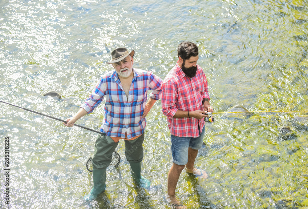 Men bearded fishermen. Weekends made for fishing. Active sunny day. Fishermen fishing equipment. Hobby sport activity. Fishermen friends stand in river. Fish normally caught in wild. Summer leisure