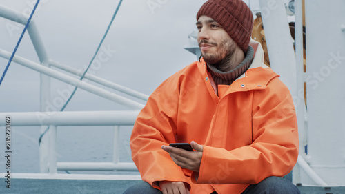 Фотография Casualy Dressed Fisherman Using Mobile Phone while Traveling on Ship