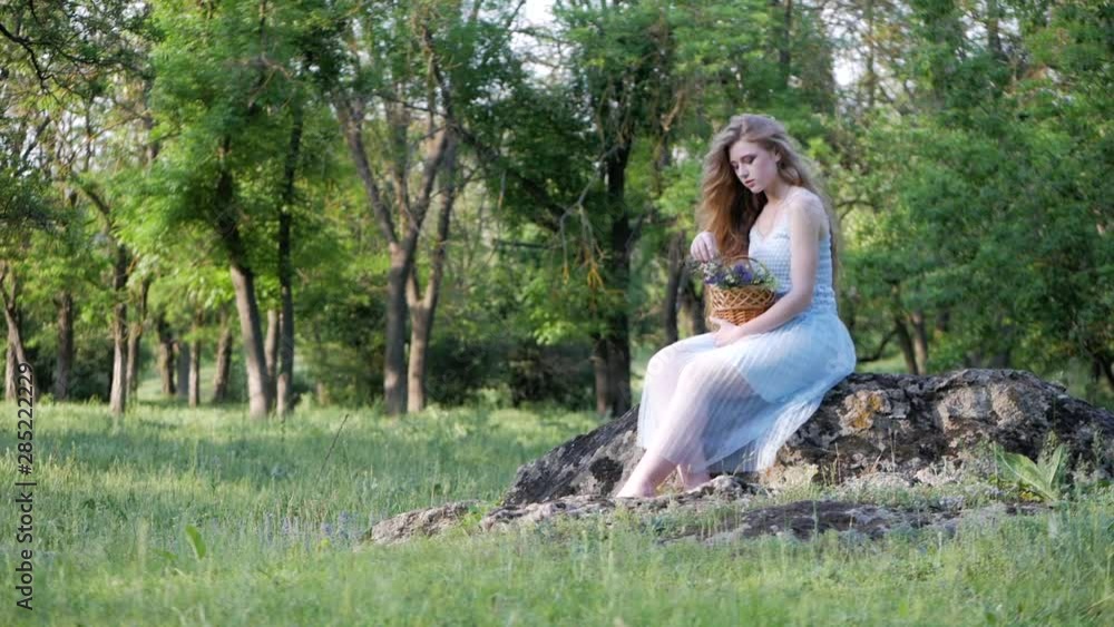 Beautiful girl in a summer dress sitting on a rock in the forest and enjoying wildflowers. Beautiful girl in a summer dress sitting on a rock in the forest and enjoying wildflowers.