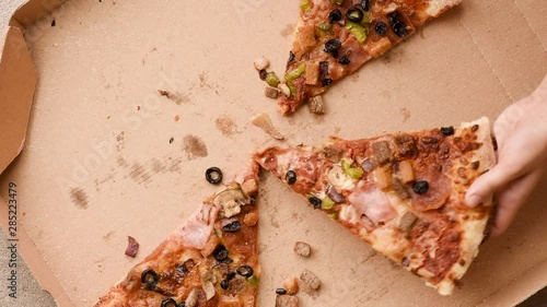Top view of hands adults and children taking pizza slices from cardboard box. Family or group of hungry unrecognizable people taking slices of delicious Italian pizza. People and food concept.