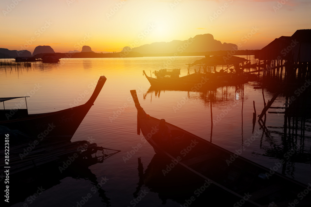 Fishermen village at sunrise..Silhouette landscape of fishermen pier and boats when the sun is coming up from the mountain with golden water reflection and twilight clear sky..