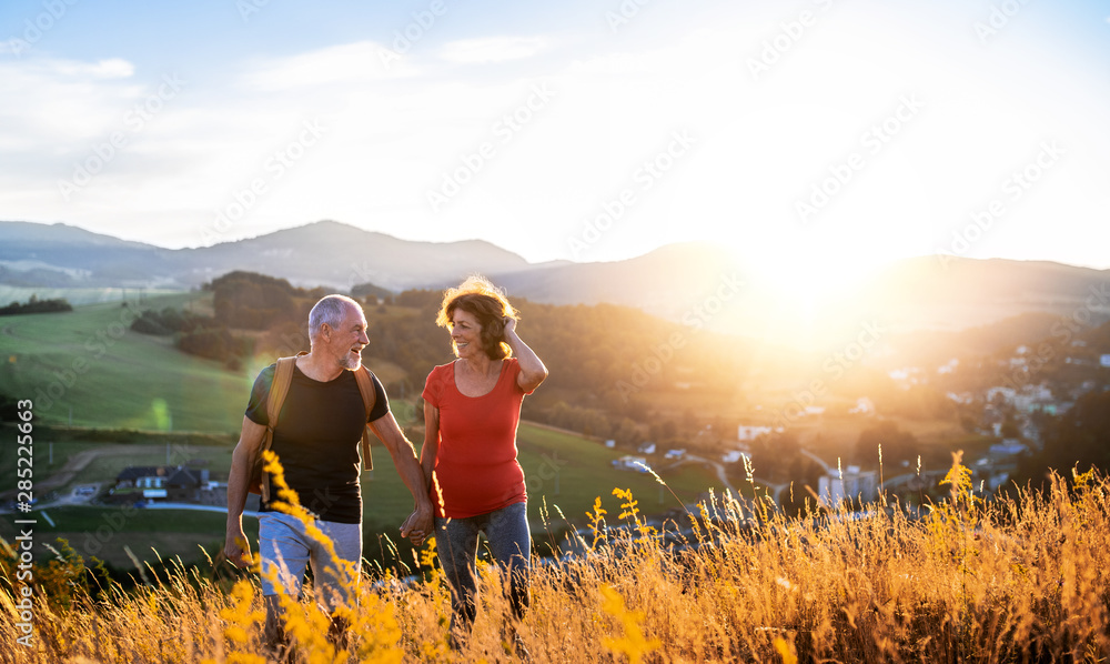 © Halfpoint - Senior tourist couple travellers hiking in nature at sunset, holding hands.