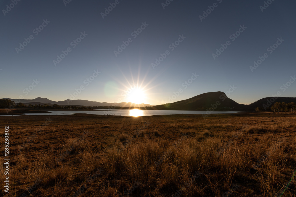 The sun sets setting over a lake creating silhouettes of the landscape in front. On a clear and sunny day in Lake Moogerah, Queensland, Australia The sun sets setting over a lake creating silhouettes of the landscape in front. On a clear and sunny day in Lake Moogerah, Queensland, Australia