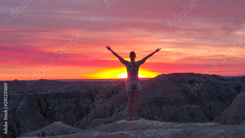Relaxed woman raising arms towards the pink sky at amazing sunset
