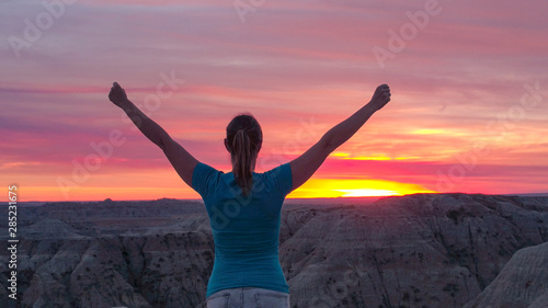 CLOSE UP: Cheerful young woman on top of the mountain celebrating at pink sunset