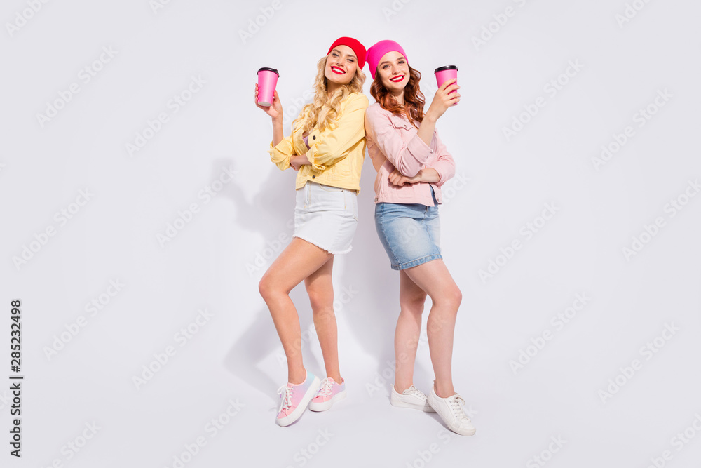 Full length photo of two pretty ladies with hot takeout beverage in hands wear casual clothes isolated white background Full length photo of two pretty ladies with hot takeout beverage in hands wear casual clothes isolated white background