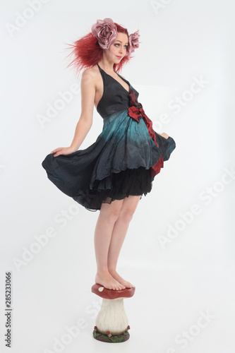 full length portrait of red haired girl wearing fairy costume, posing on a white studio background.