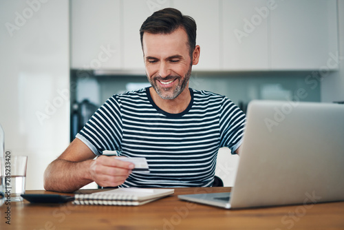 Smiling man using credit card to do online shopping on laptop at home