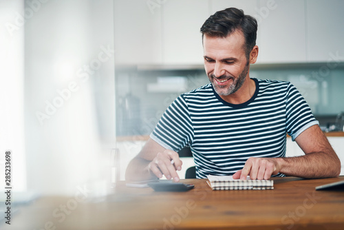 Smiling man using notebook and calculator to manage home budget